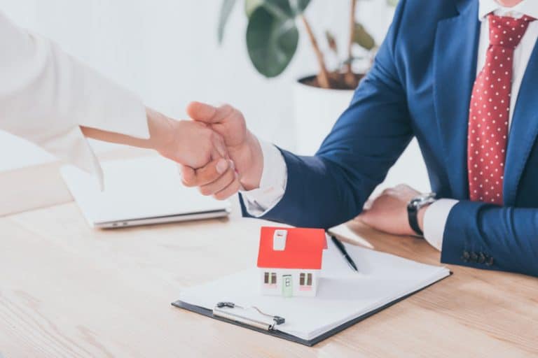 partial view of businessman and client shaking hands near house model on table