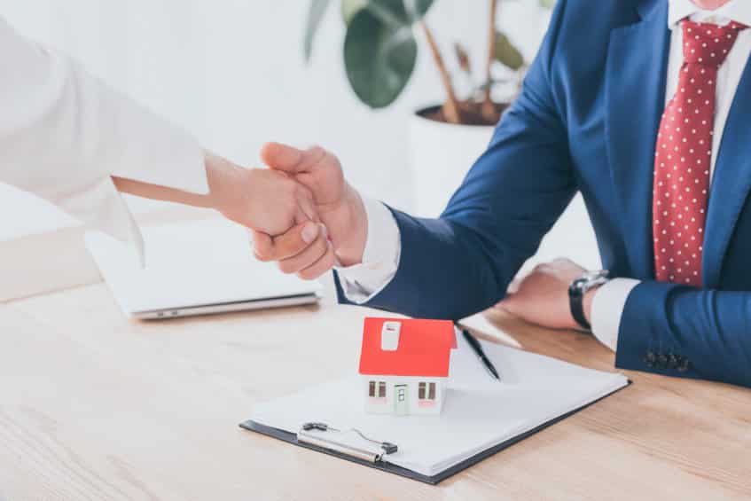 partial view of businessman and client shaking hands near house model on table